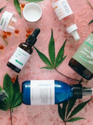 Flat lay of CBD products with cannabis leaves on pink fabric, perfect for wellness theme.
