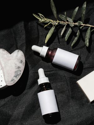 Flat lay of skincare products with gua sha and leaves on black textile. Ideal for beauty and wellness visuals.
