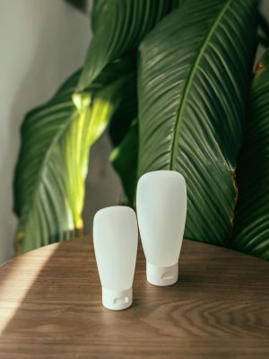 Two white cosmetic containers on a wooden table with green leaves background.
